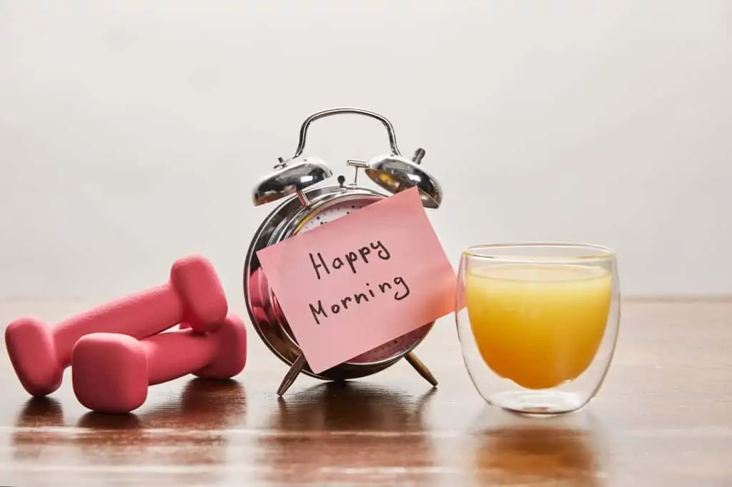 picture of pink weights, alarm clock, and orange juice. decorative image to illustrate healthy concept in an article about how to make exercise a habit.