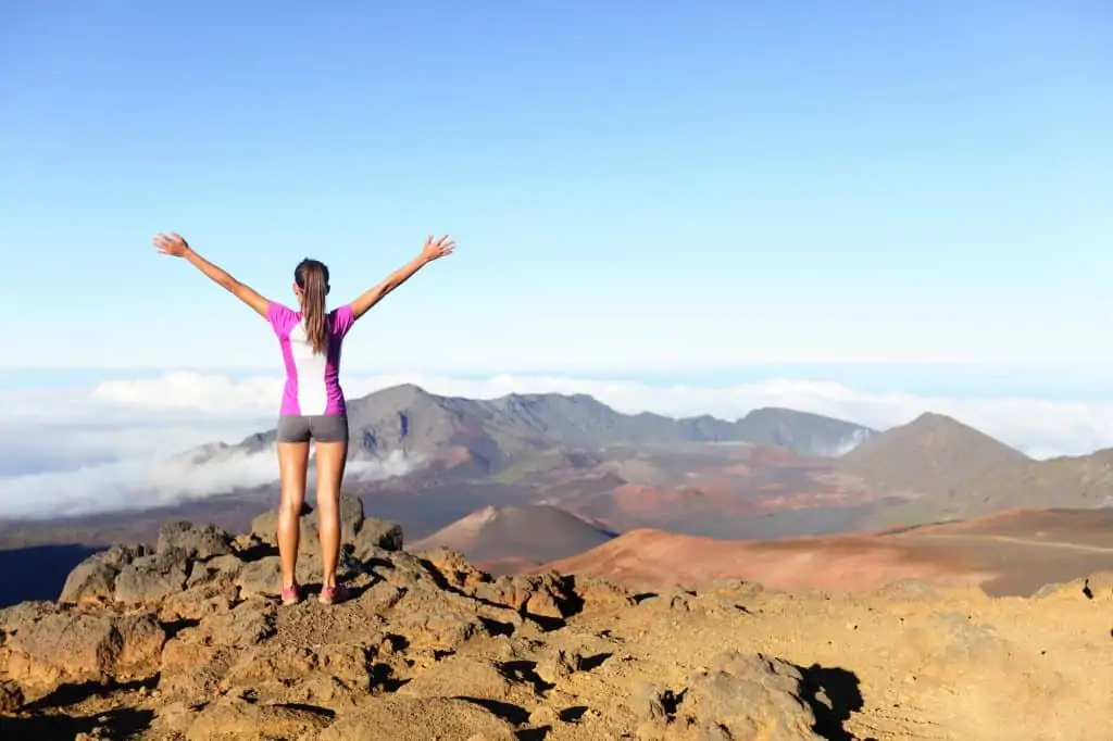 woman standing on a mountain with her arms in the air symbolizing success
