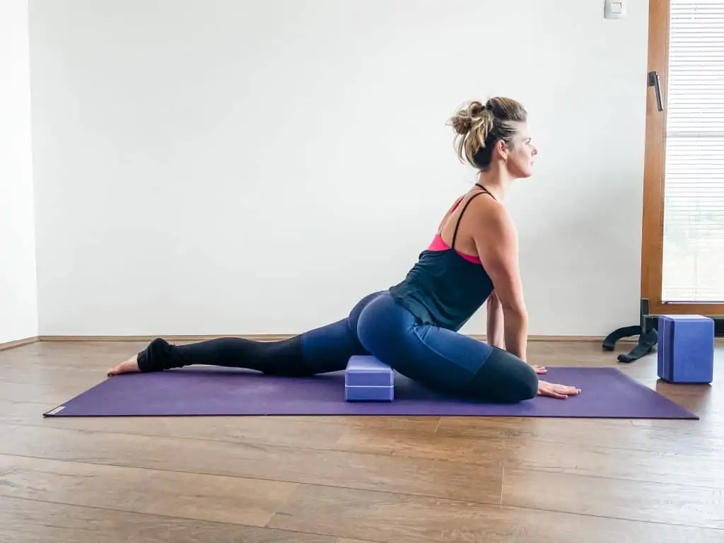 woman on a yoga mat demonstrating pigeon pose with a yoga block