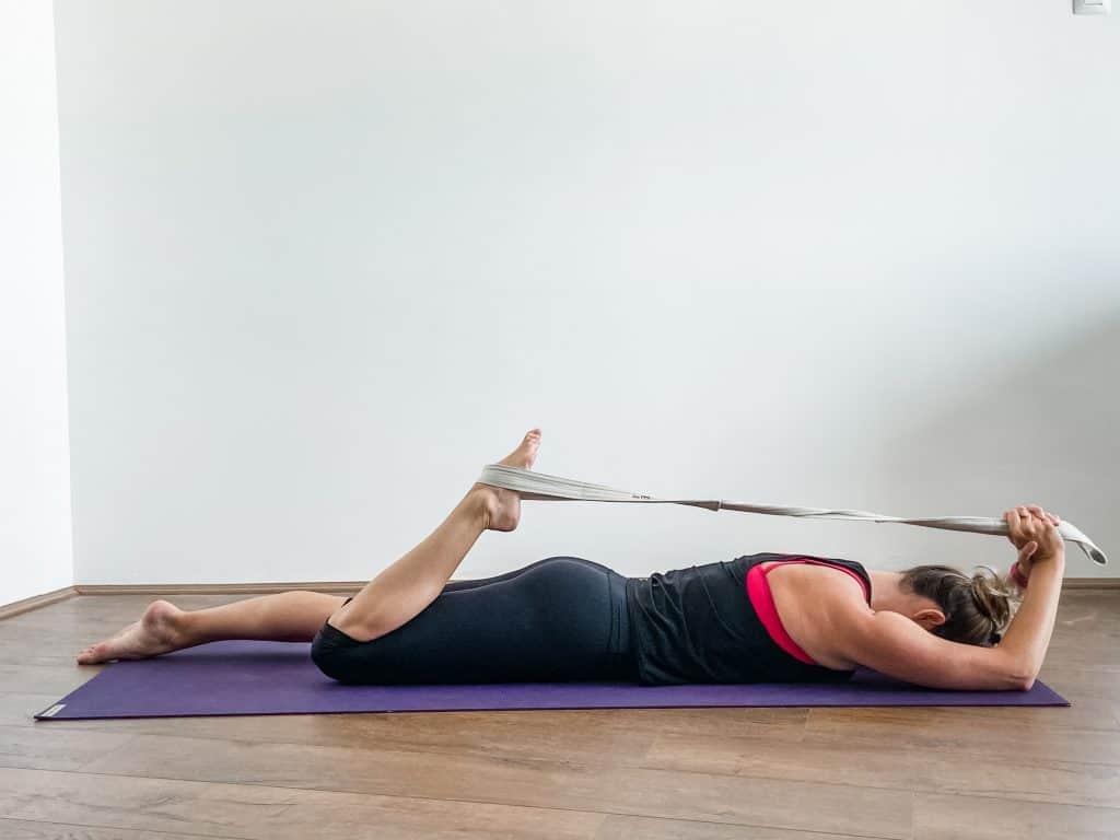 woman on a yoga mat performing a prone quad muscle stretch