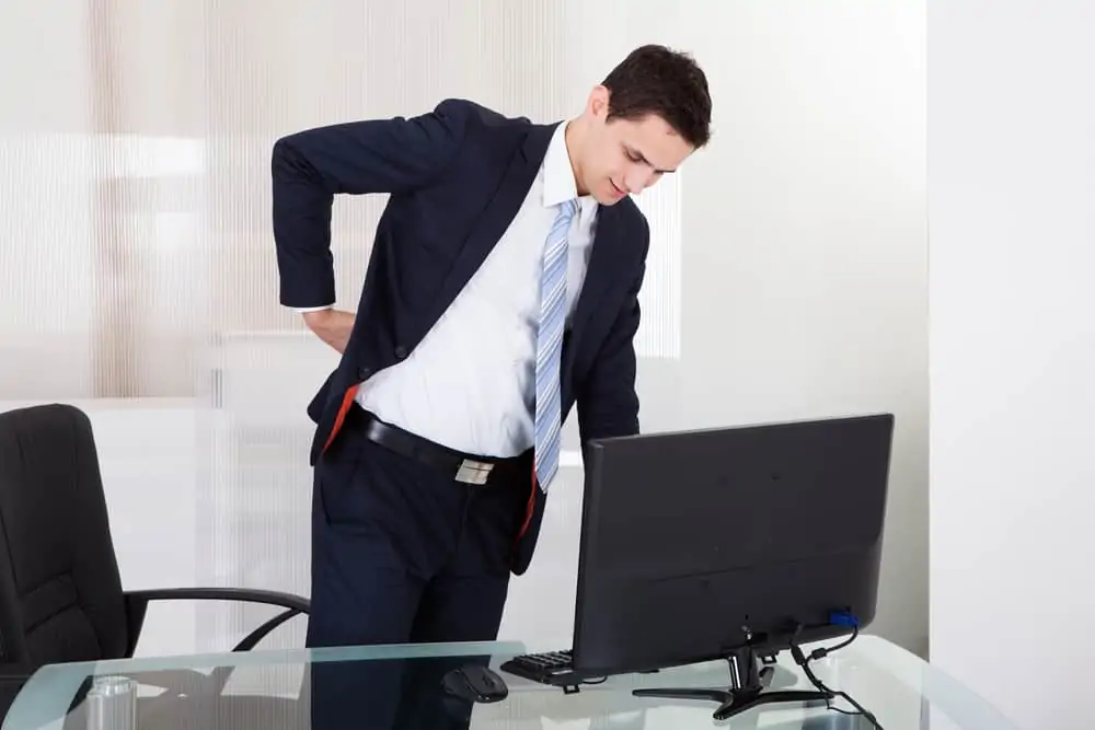 man at a desk with a backache. decorative image in an article about standing desk pros and cons