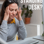 woman seated working at a desk in pain holding her head with text overlay do you need a standing desk?