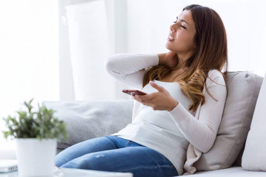 woman sitting on a couch using a mobile phone rubbing her neck in pain how to avoid text neck