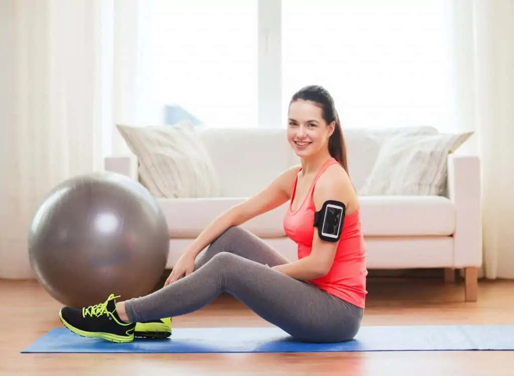 woman at home sitting on an exercise mat next to an exercise ball best physical therapy equipment for home