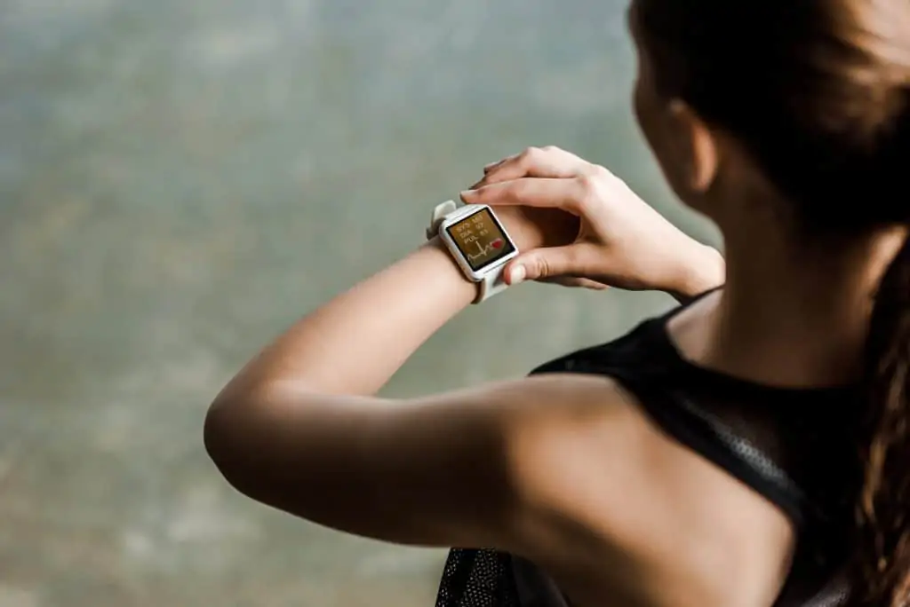 woman looking down at her fitness watch, a decorative image in an article about the best gym bag accessories for beginners