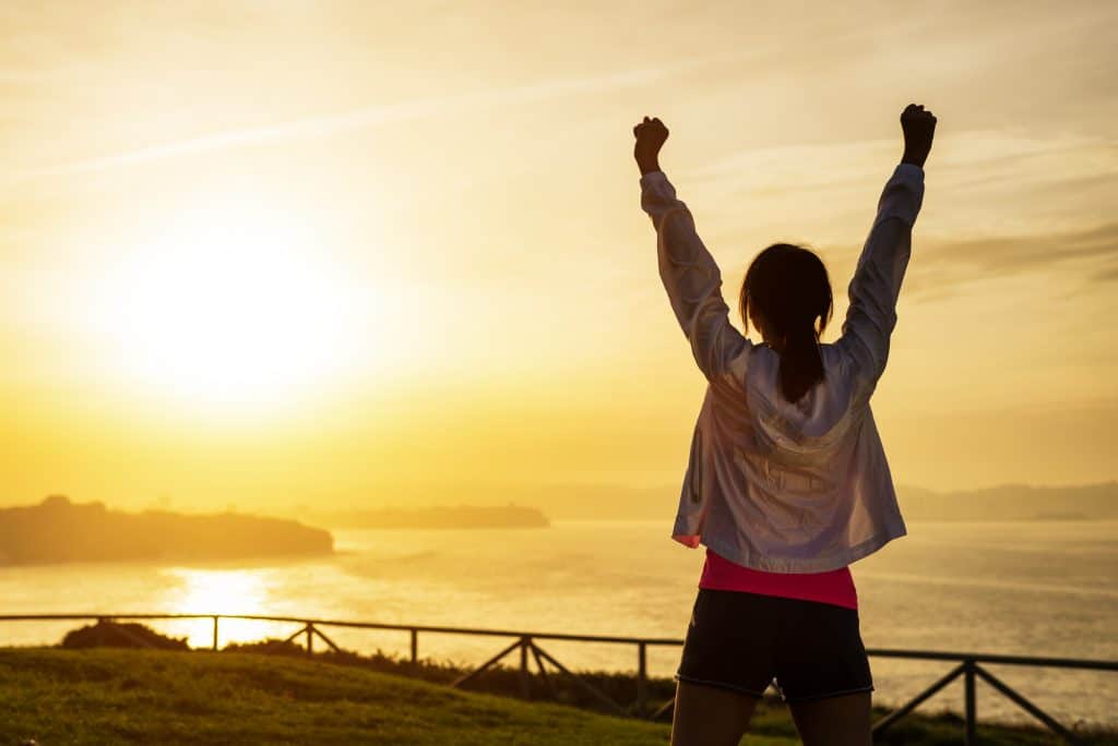 woman outdoors with arms up in success, a decorative image in an article about how to be more active