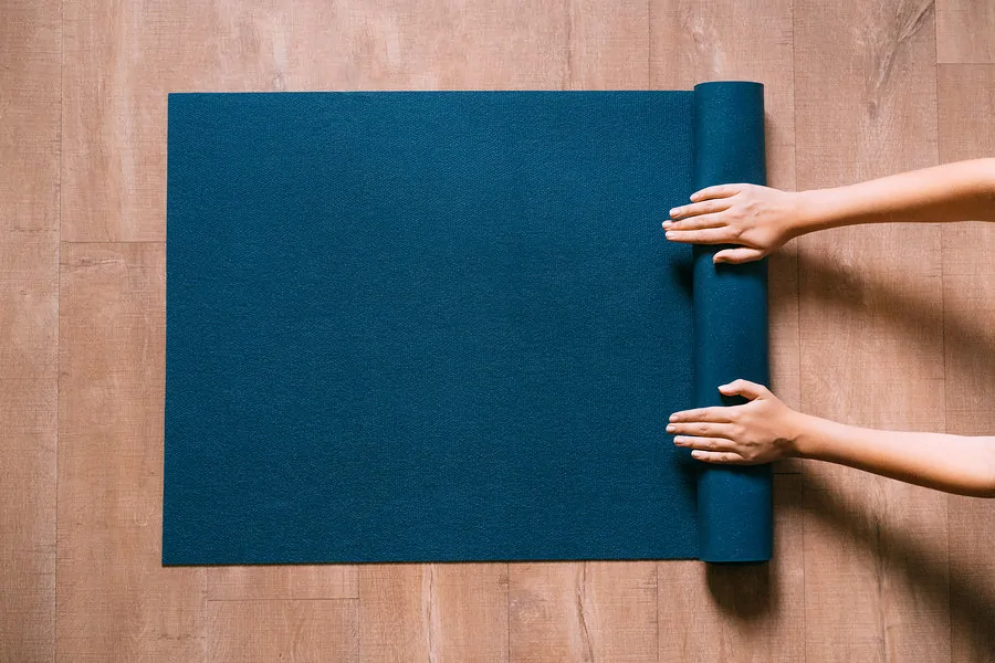 woman's hands unrolling a yoga mat on the floor