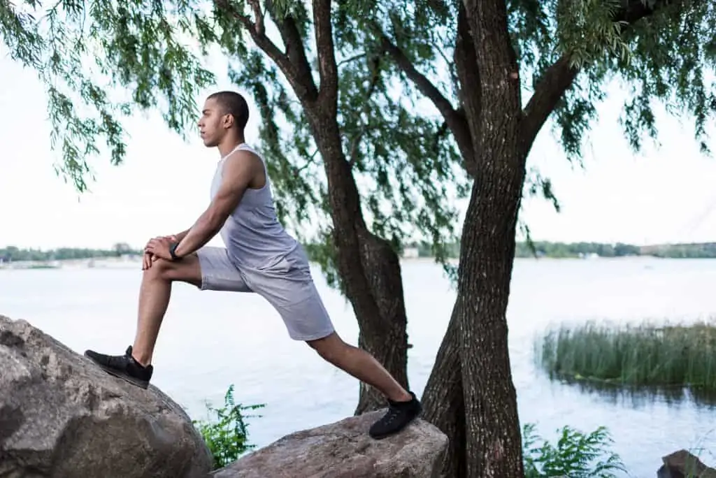 a man stretching his hip flexors by a river while working out