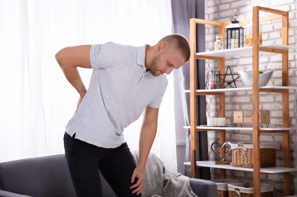 a man holding his back in pain as a decorative image for an article about what to avoid with sciatica