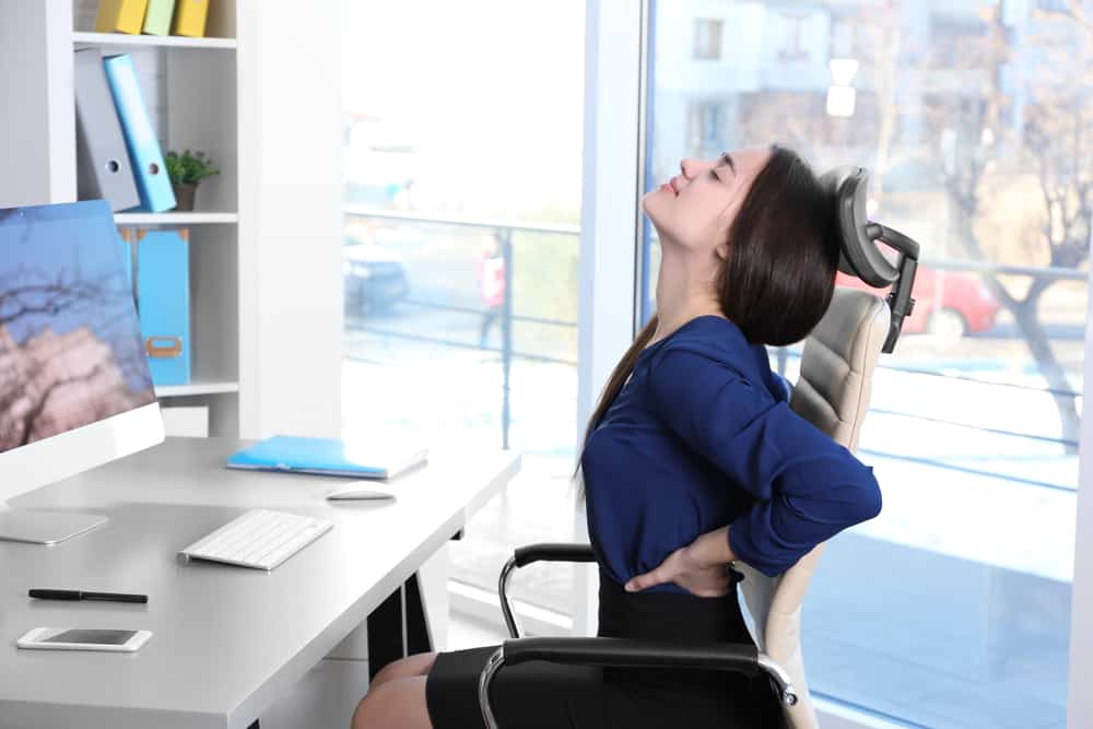 woman sitting at a desk stretching her back. decorative cover image for an article about how to improve your posture