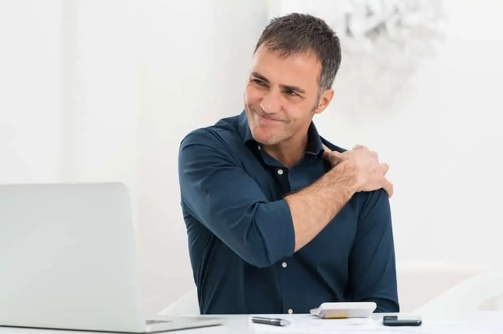 a man holding his shoulder in pain. decorative image for an article about shoulder impingement pain.