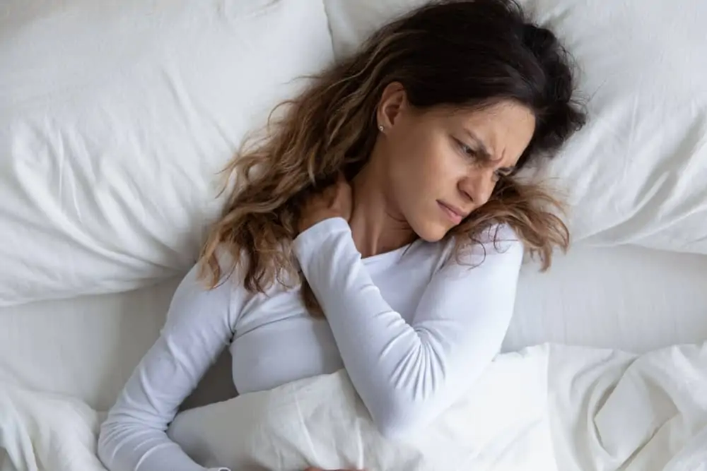 woman in bed holding her neck symbolizing neck pain from sleeping wrong