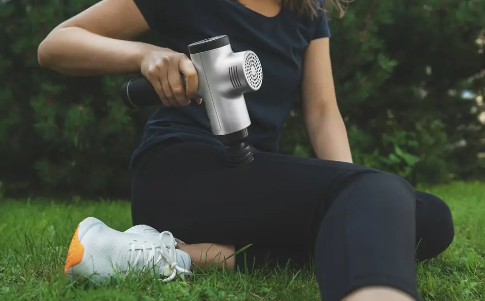 woman using a massage gun on her leg after a workout