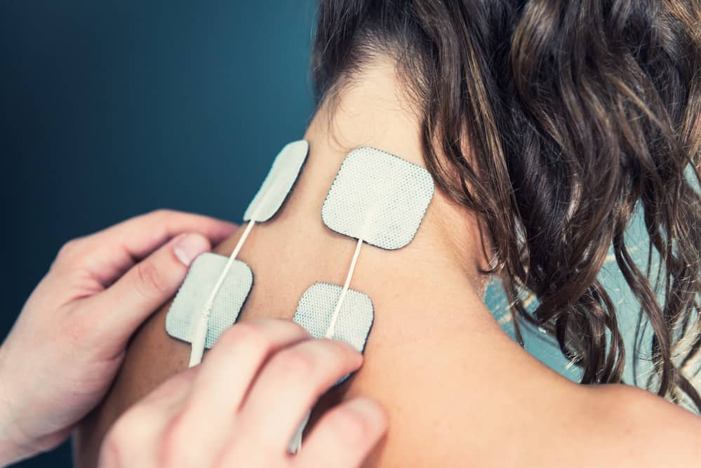 a physical therapist placing tens electrodes on a woman's neck and upper back