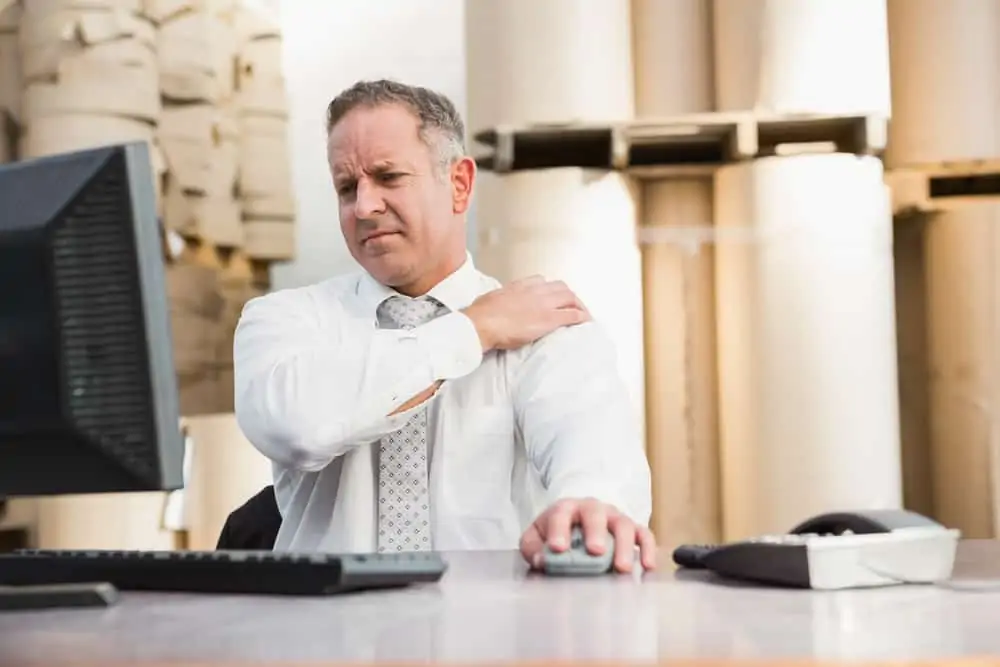 man working at a desk holding his shoulder in pain