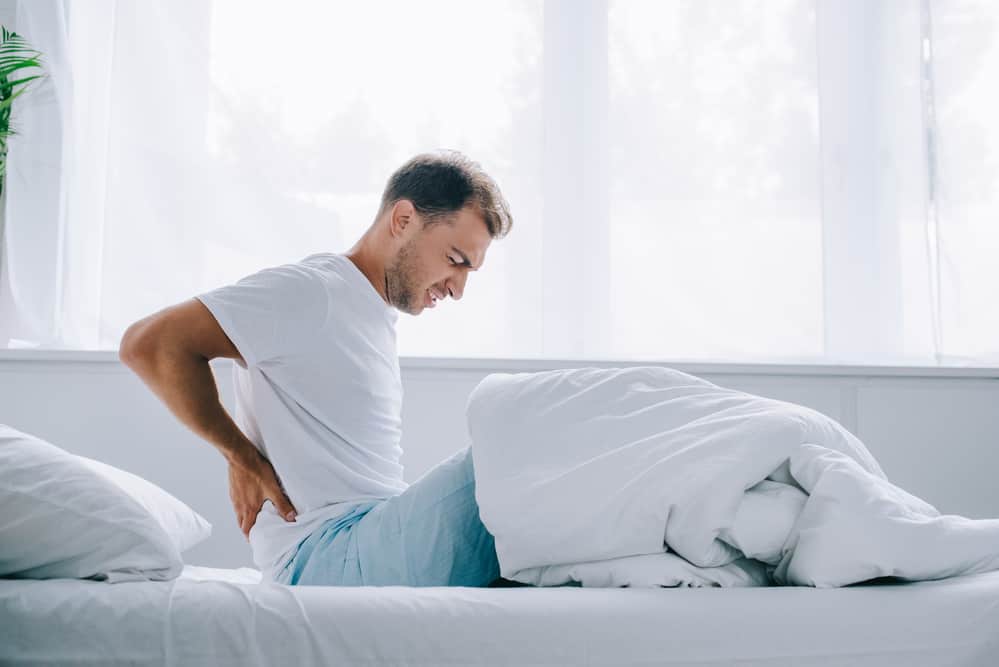 a man sitting up in bed holding his back in pain