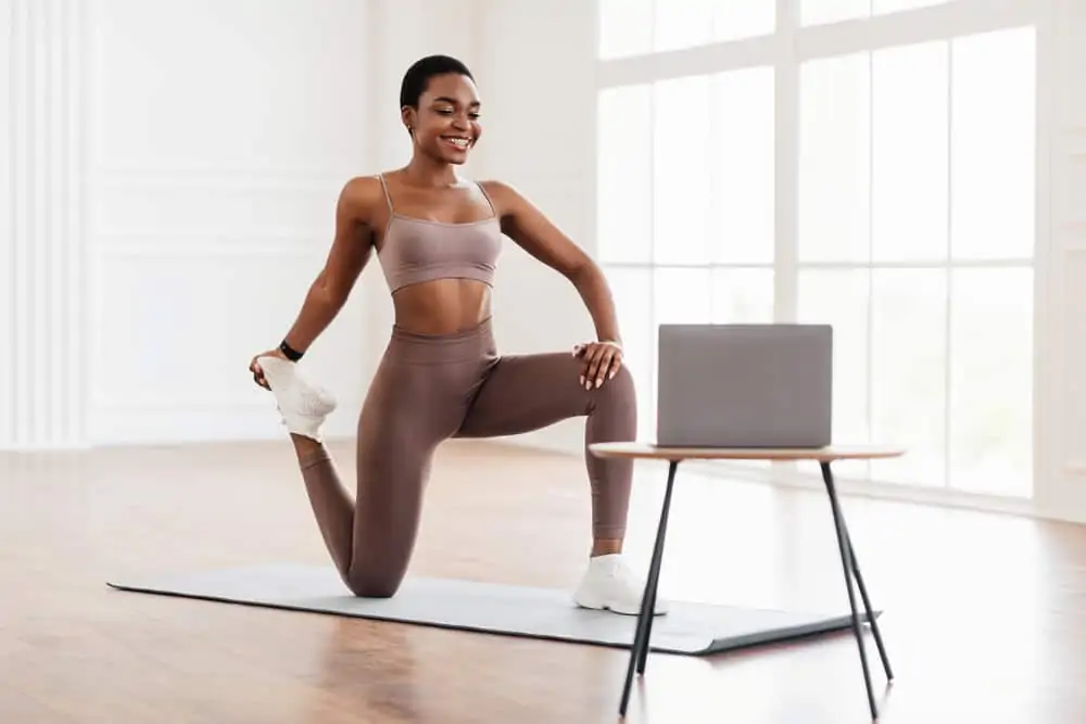 african american woman stretching on a yoga mat while watching a computer