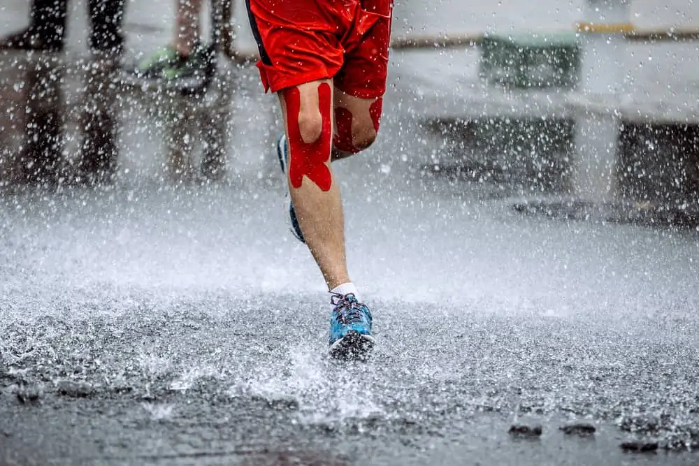 athlete running in the rain with kinesiology tape on his knees