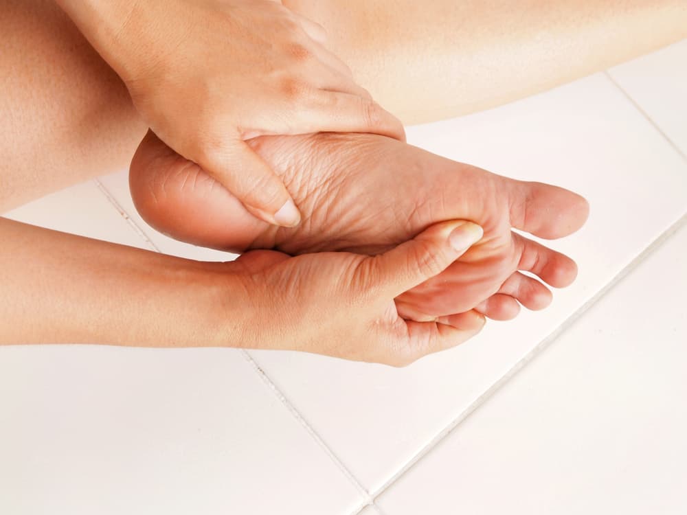 woman holding her foot in pain, a decorative image for an article about orthotics vs. insoles