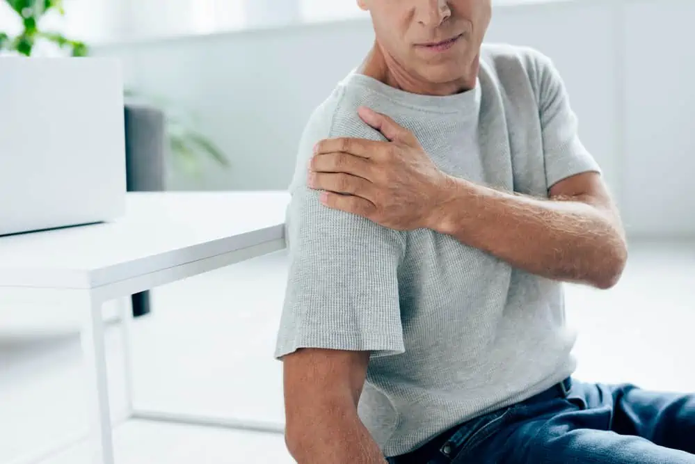 man holding his shoulder in pain - decorative for an article about shoulder impingement vs. frozen shoulder